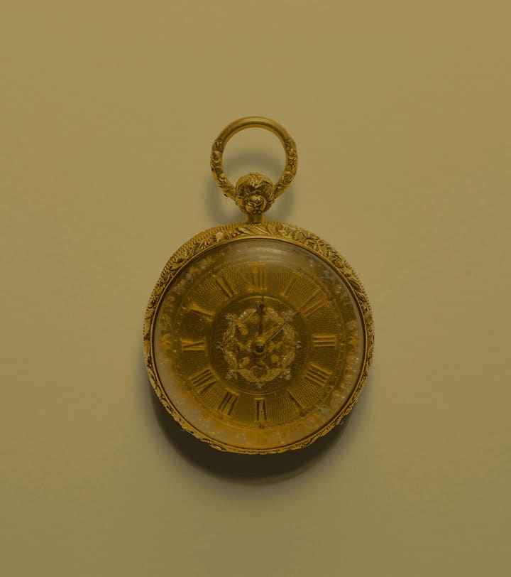 A gold pocket watch with an engraved case on a plain background