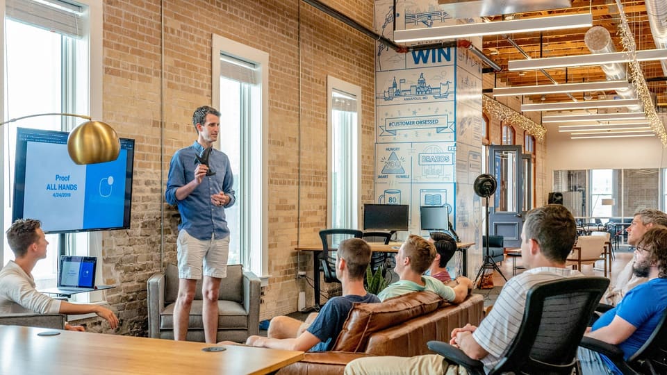 A team meeting in a converted-warehouse office, with a presenter addressing colleagues seated around a table